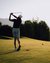 Golfer schlägt Ball auf sonnigem Golfplatz mit Bäumen und Bergen im Hintergrund