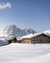 Skiers by a mountain cabin in snowy landscape with clear sky and mountains