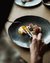 Person eating dish with egg and bacon on black plate on wooden table