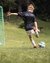 Child kicking soccer ball towards goalkeeper at football camp