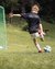 Child kicking soccer ball towards goalkeeper at football camp