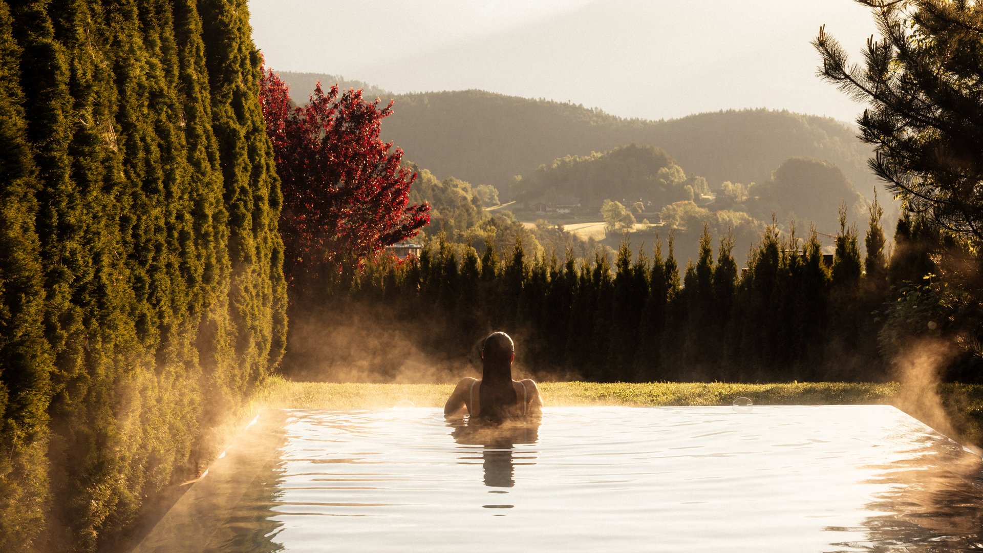 Person relaxing in heated pool with mountain and tree view