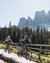 Due ciclisti pedalano su un sentiero di montagna con recinzione di legno e montagne sullo sfondo