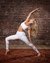 Frau in weißer Sportkleidung macht Yoga-Pose auf Teppich vor Backsteinwand