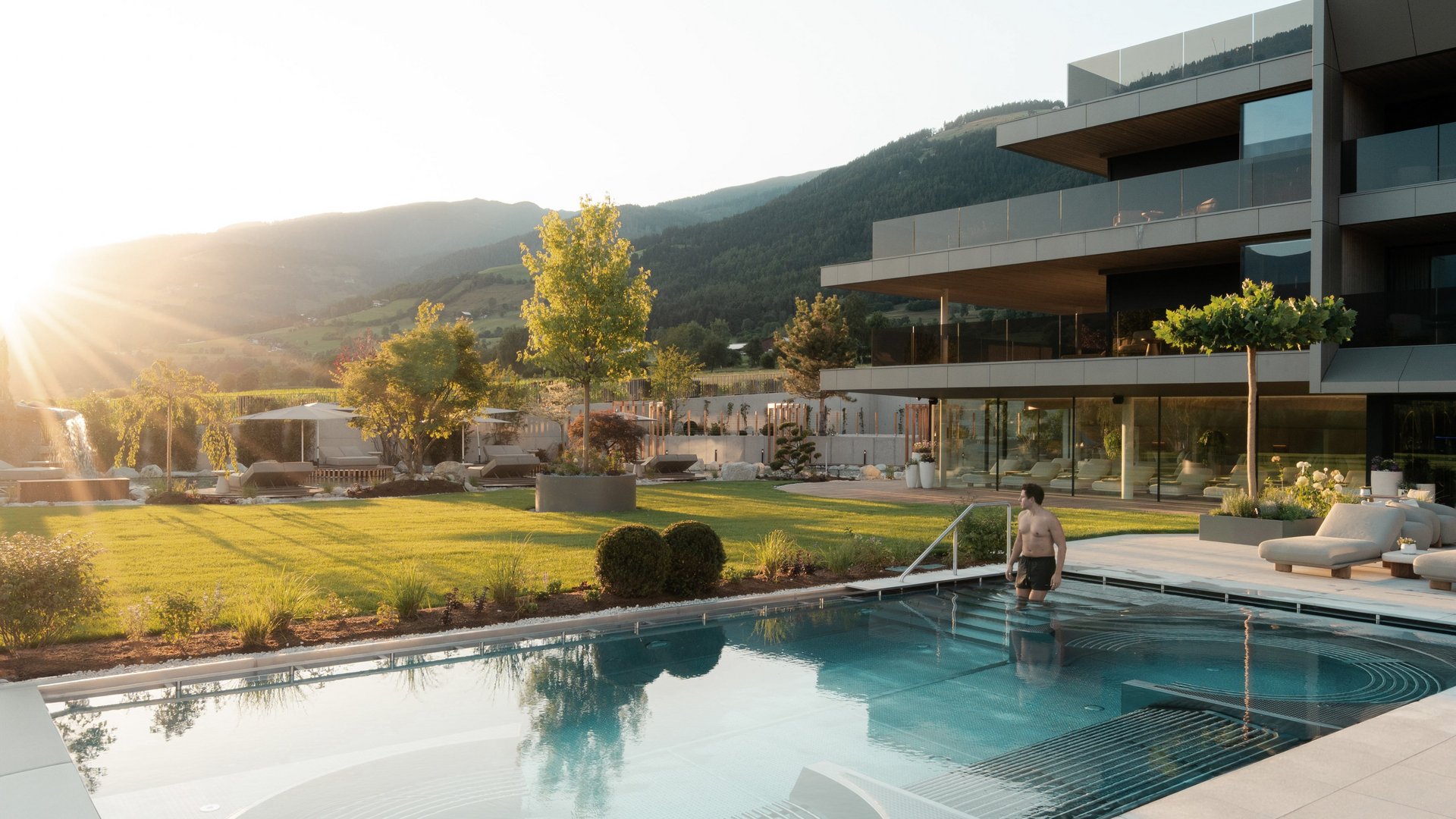 Uomo entra in piscina esterna moderna accanto a edificio al tramonto
