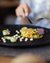 Finely plated vegetable terrine on black plate with wine and cutlery
