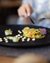 Tartare di verdure finemente impiattato su piatto nero con vino e posate