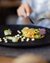 Finely plated vegetable terrine on black plate with wine and cutlery