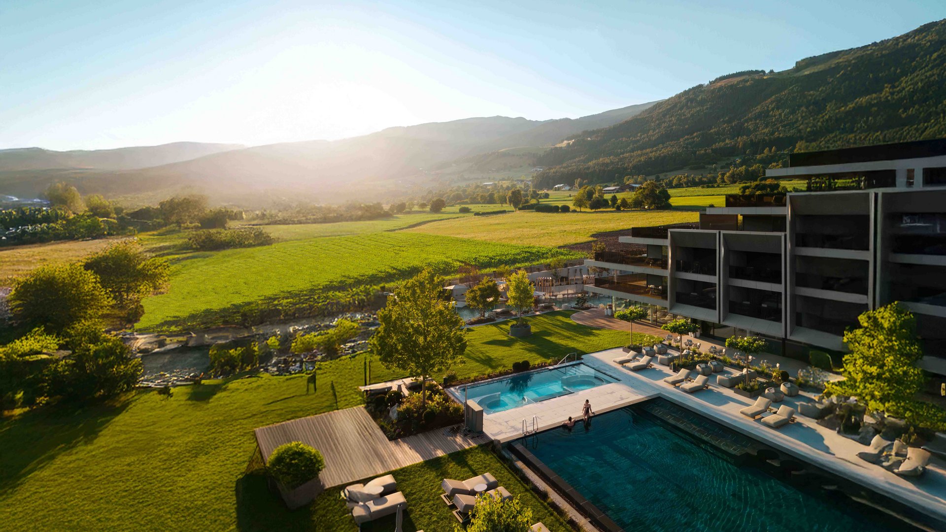 Sonniger Blick auf Pool, Wiese und Berge bei modernem Hotel