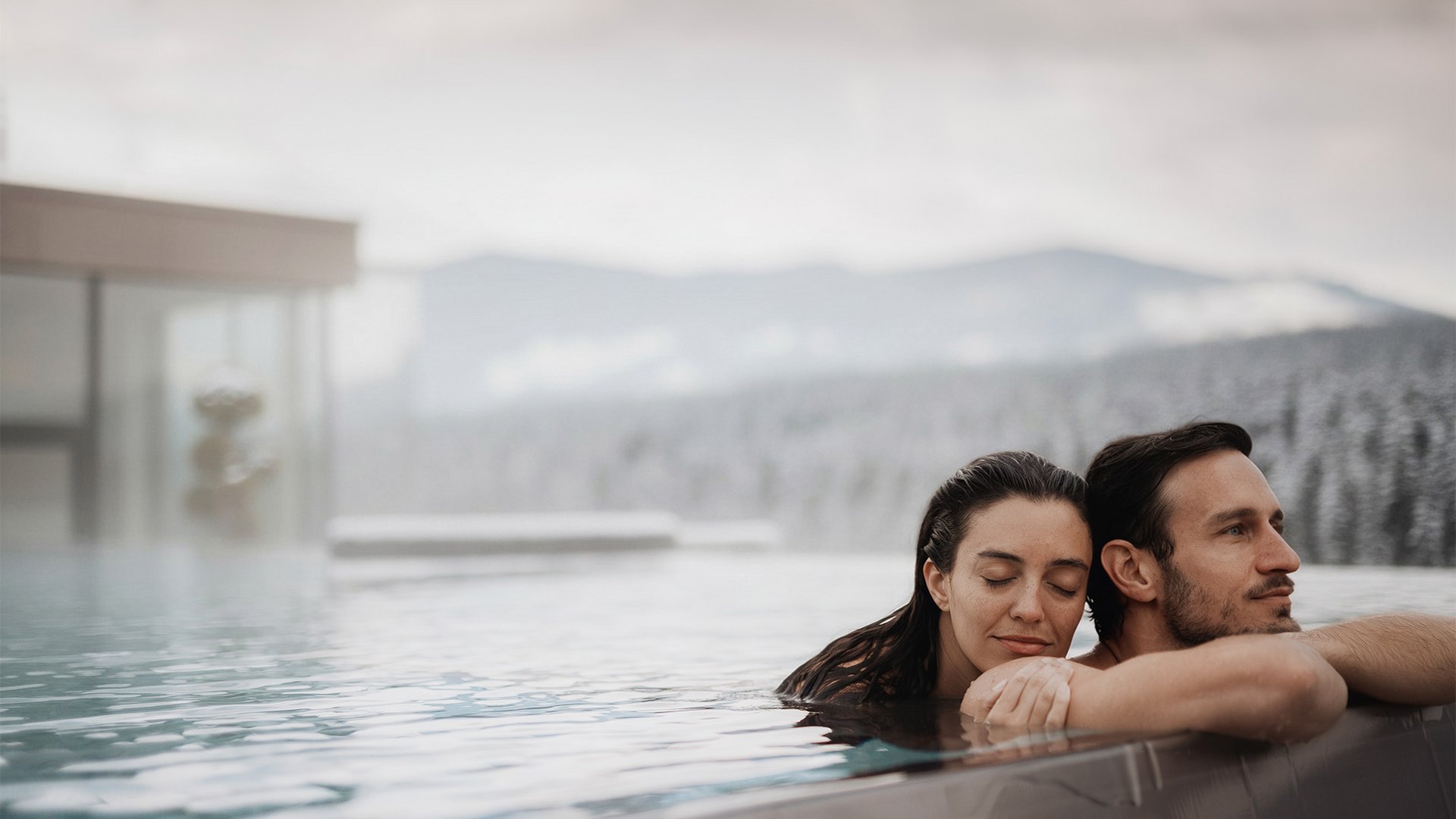Paar entspannt sich im Außenpool mit verschneiten Bergen im Hintergrund