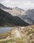 Zwei Radfahrer auf einem Bergweg neben einem See mit Bergen im Hintergrund