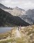 Two cyclists on a mountain trail beside a lake with mountains in the background