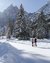 Due persone camminano su un sentiero innevato tra abeti e montagne