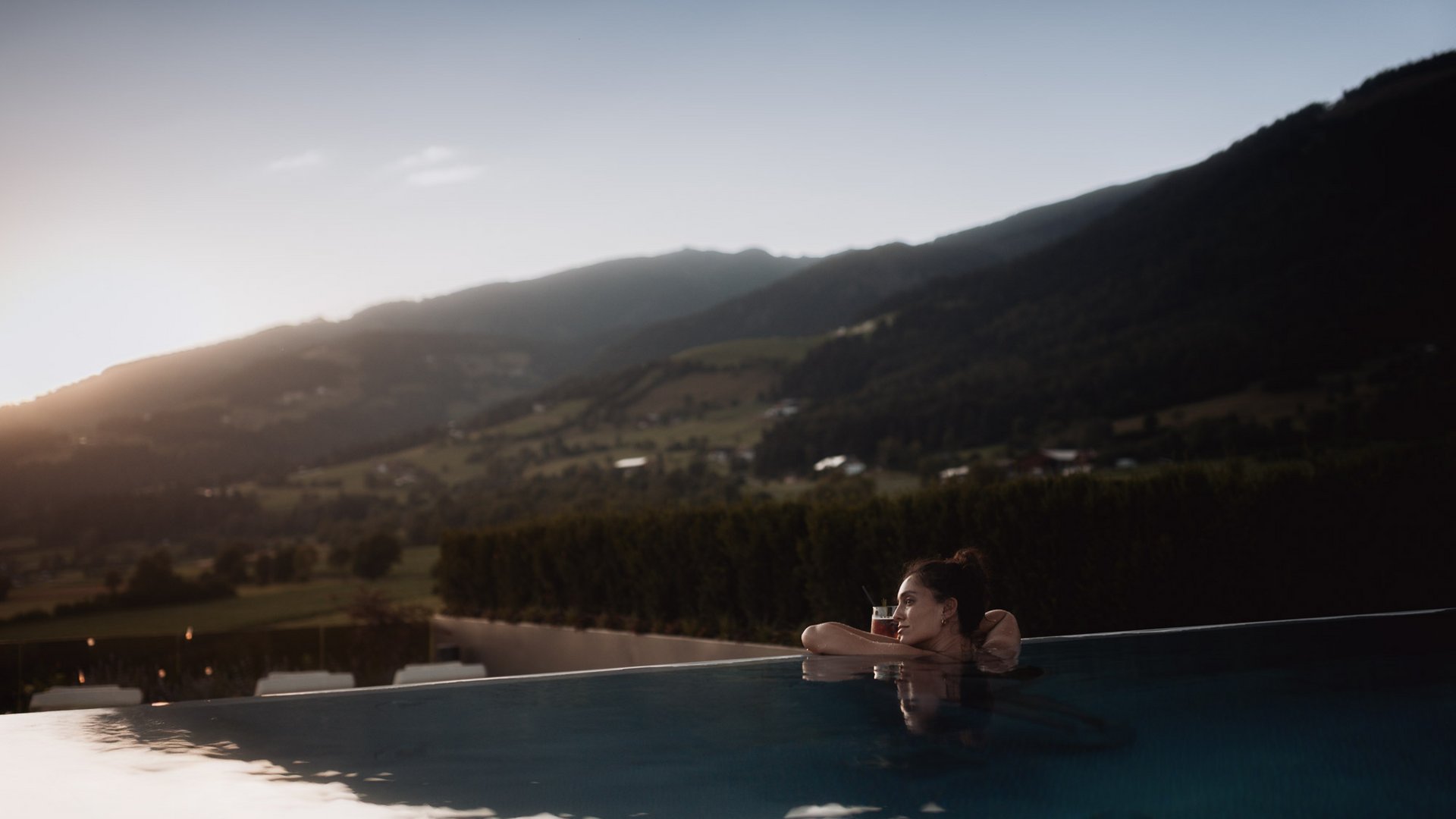 Woman relaxing in pool at sunset with mountain view