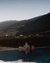 Frau entspannt im Pool bei Sonnenuntergang mit Bergblick