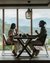 Couple sitting at dining table with wine glasses by large window with mountain view